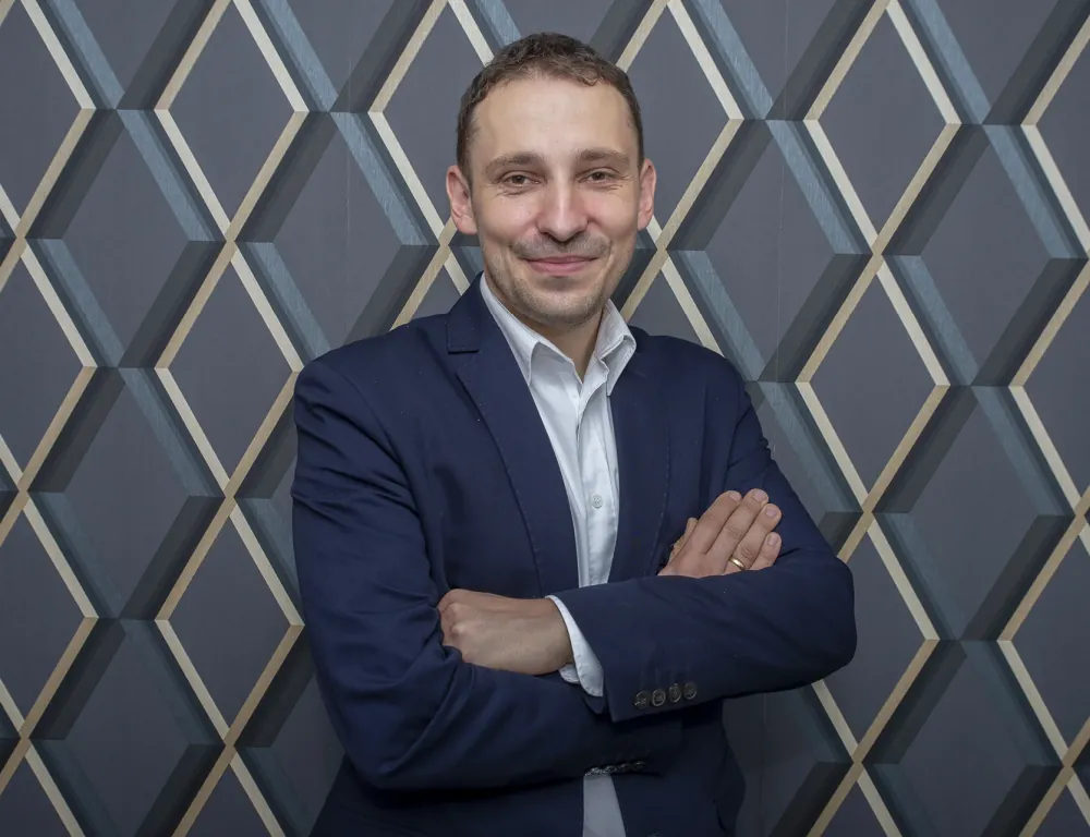 Ilustracja przedstawia mężczyznę stojącego przy ściance. Jest to Leszek Chojnicki.